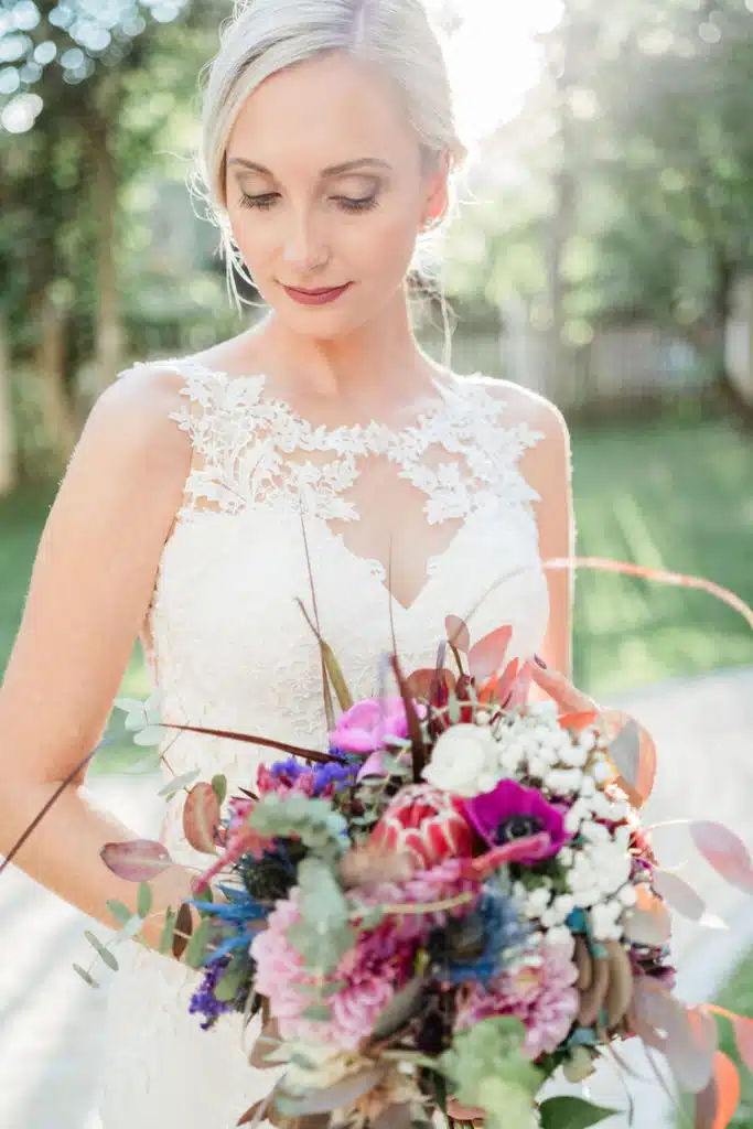 Hochzeitsfoto einer eleganten Braut mit mondernem Blumenstrauß bei Sonnenuntergang
