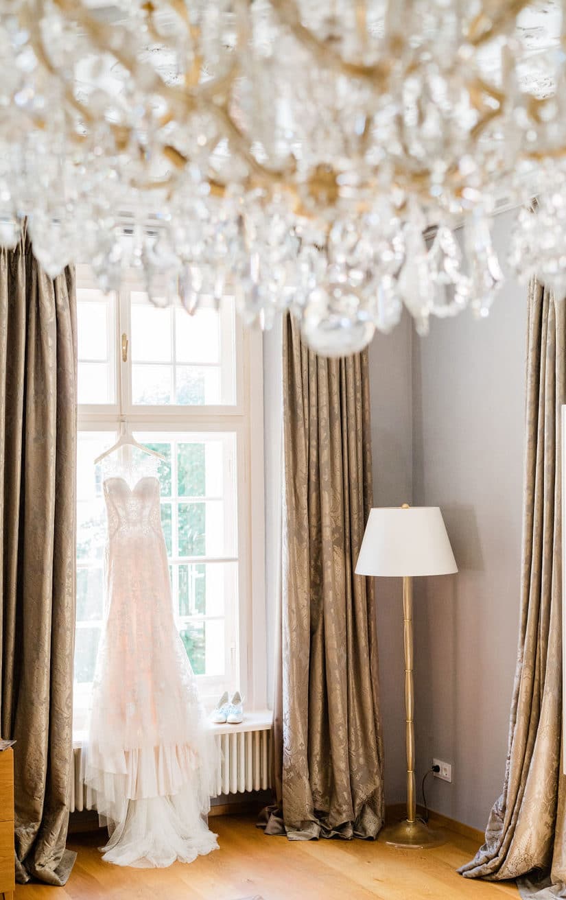 elegantes Brautkleid hängt am Fenster mit glamourösem Kristallluster